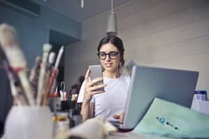 Dame på kontor, som ser på mobiltelefonen.
