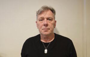 Jan har på seg en sort genser. Det er lys bakgrunn på bildet.