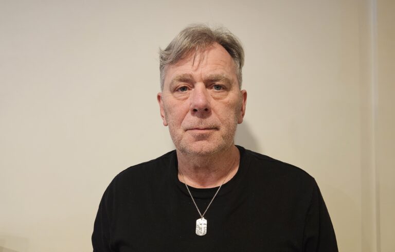 Jan har på seg en sort genser. Det er lys bakgrunn på bildet.